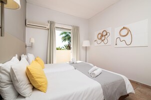 Habitación de hotel con cama, dos lámparas de pared, una ventana con cortinas y vistas a palmeras.