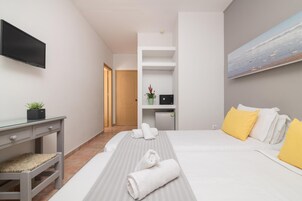 Una habitación de hotel con cama, escritorio, televisión, una planta pequeña y un cuadro en la pared.