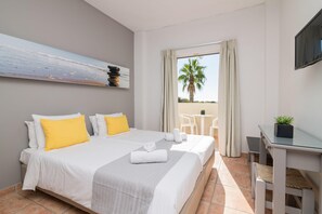 A hotel room with a bed, a desk, a TV, a painting, and a view of the beach. - Cavo Doro Hotel (KALAMAKI)
