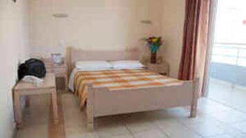 Una habitación de hotel con cama, mesita de noche y velador con lámpara.