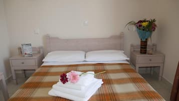 A neatly made bed with a plaid bedspread, two white pillows, and a folded towel with a flower on a bedside table.