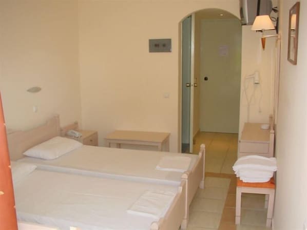 A hotel room with a bed, bedside table, and a small table with a chair. There is a door leading to a bathroom. - Theonia (Kos)