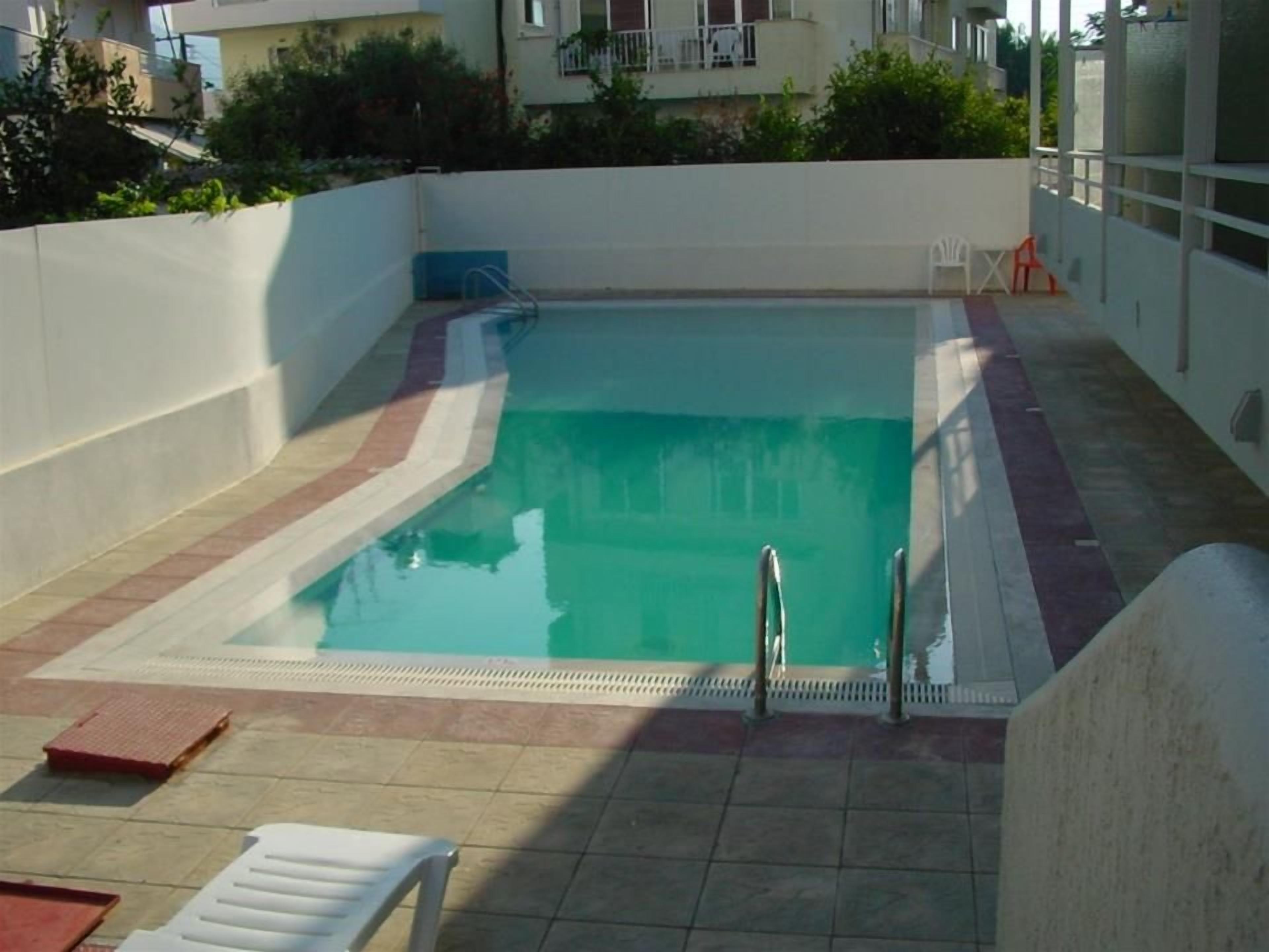Une piscine rectangulaire avec une terrasse carrelée, une échelle en métal et quelques chaises longues.