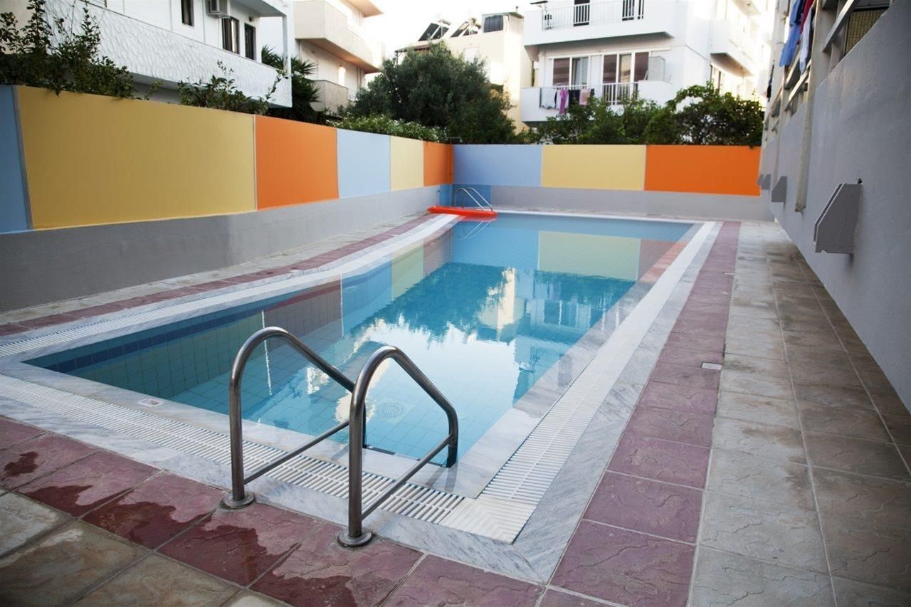 Une piscine avec un escalier en métal, entourée d’une terrasse carrelée et d’un mur aux couleurs vives.