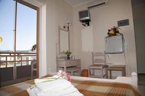 Een hotelkamer met een bed, bureau, stoel, kaptafel met spiegel en een televisie.