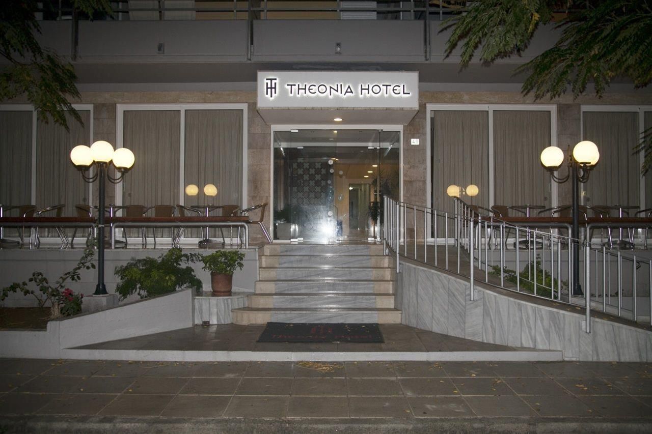 La entrada del Hotel Theonia, con una escalera de mármol, plantas en macetas y una barandilla de metal.