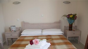 A neatly made bed with a plaid bedspread, two white pillows, and a folded towel with a flower on a bedside table. - Theonia (Kos)