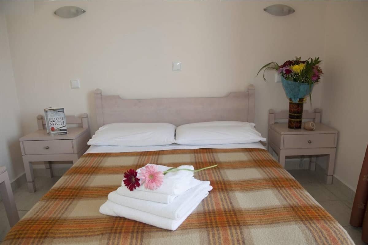 A neatly made bed with a plaid bedspread, two white pillows, and a folded towel with a flower on a bedside table.