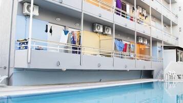 Un edificio de varios pisos con balcones, unidades de aire acondicionado y una piscina.
