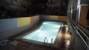A rectangular swimming pool with a tiled deck, surrounded by a low wall with colorful panels. - Theonia (Kos)