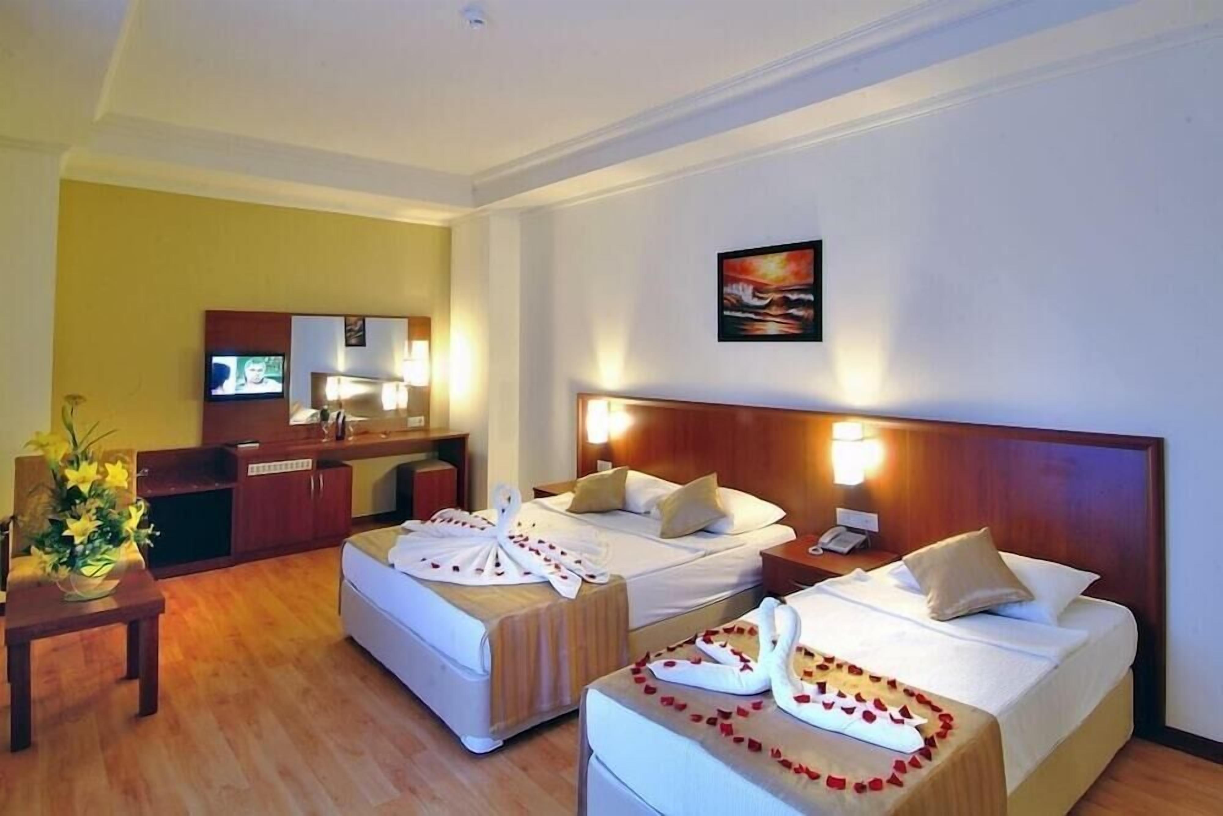 Ein Hotelzimmer mit zwei Betten, einem Schreibtisch, einem Fernseher und einem Bild an der Wand.