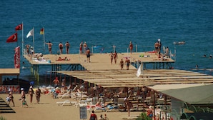 Ein Strand mit einer Seebrücke, Liegestühlen und Flaggen.