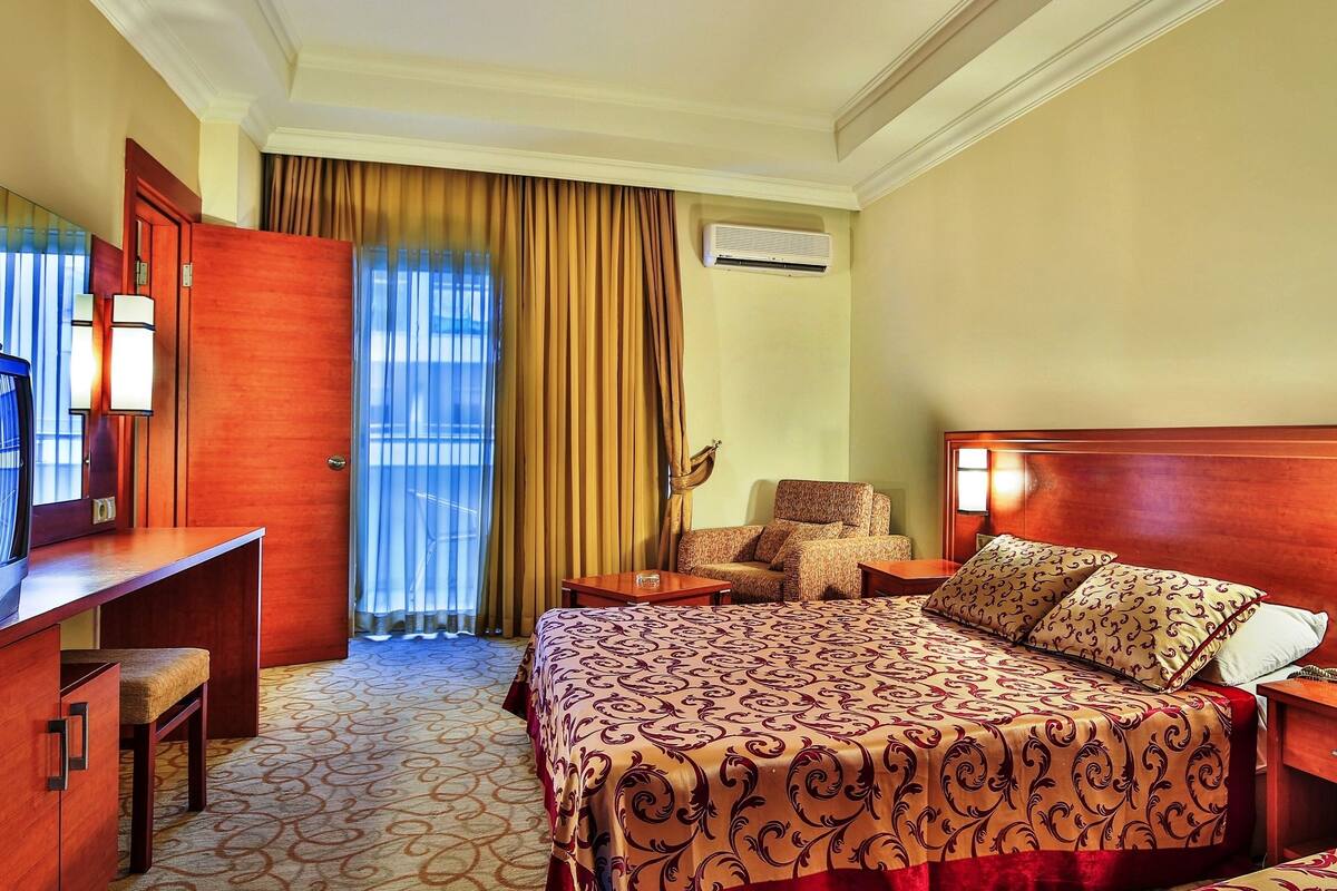A hotel room with a bed, a desk with a television, a chair, and a nightstand with a phone.