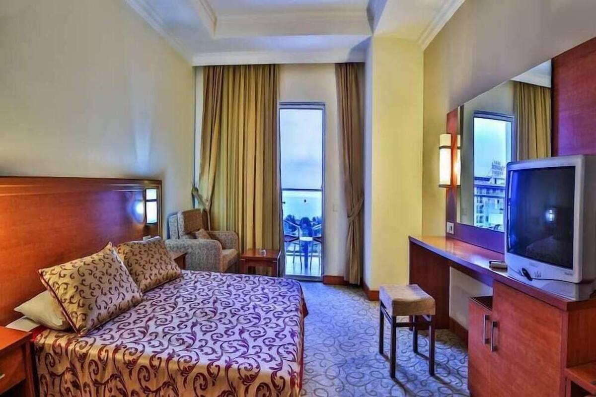 A hotel room with a large bed, a television, a desk, and a balcony with a view.