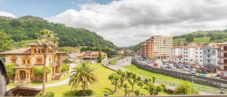 A view of a town with a mix of traditional and modern buildings, a river, and green hills in the background.
