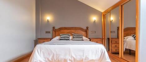 A bedroom with a wooden bed, two bedside tables with lamps, a large mirror, and a wardrobe.