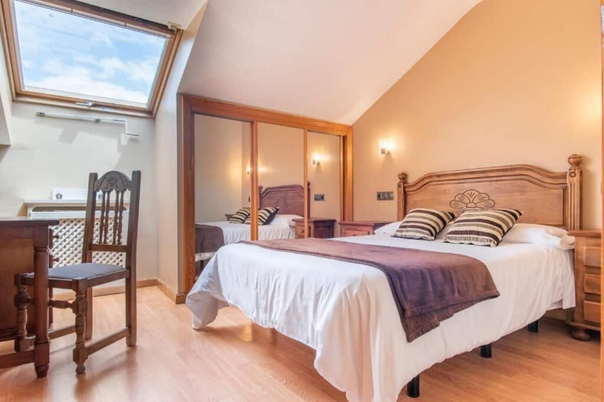 Ein Schlafzimmer mit einem großen Bett, einem Holzstuhl, einem Schreibtisch und einem Dachfenster.