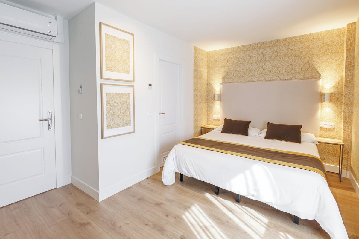 Ein Schlafzimmer mit einem großen Bett, Nachttischlampen, gerahmten Bildern an der Wand und einer Tür mit Griff.