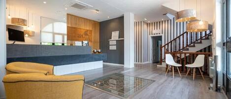 A modern reception area with a counter, seating, and a staircase leading to upper floors.