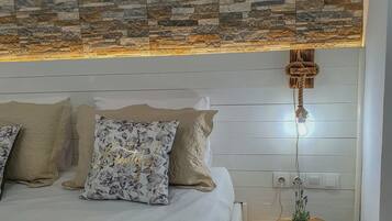 A bedroom with a stone-patterned headboard, a bed with white linens, and a bedside table with a potted plant.