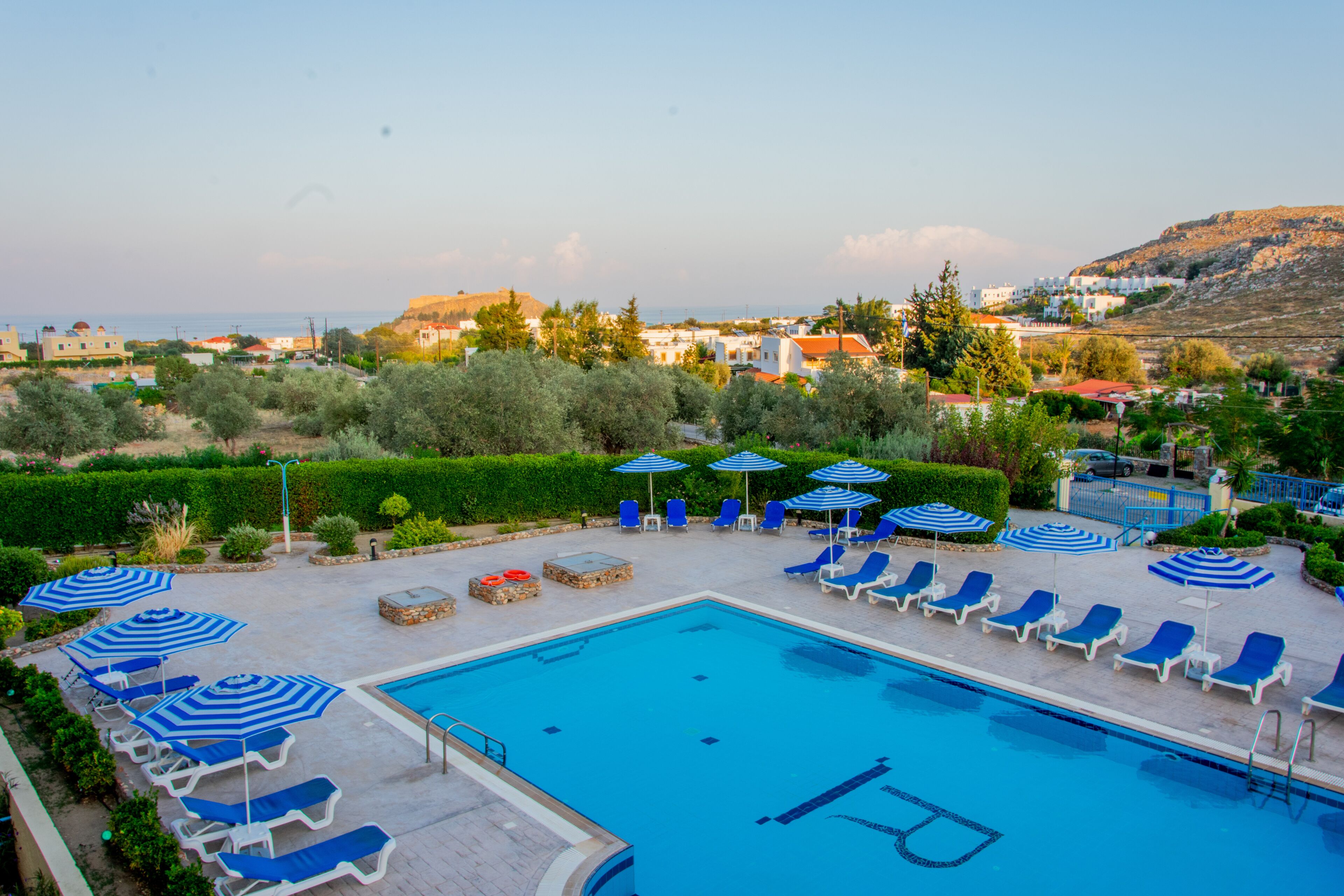 A swimming pool with lounge chairs and umbrellas, surrounded by greenery and buildings in the background.