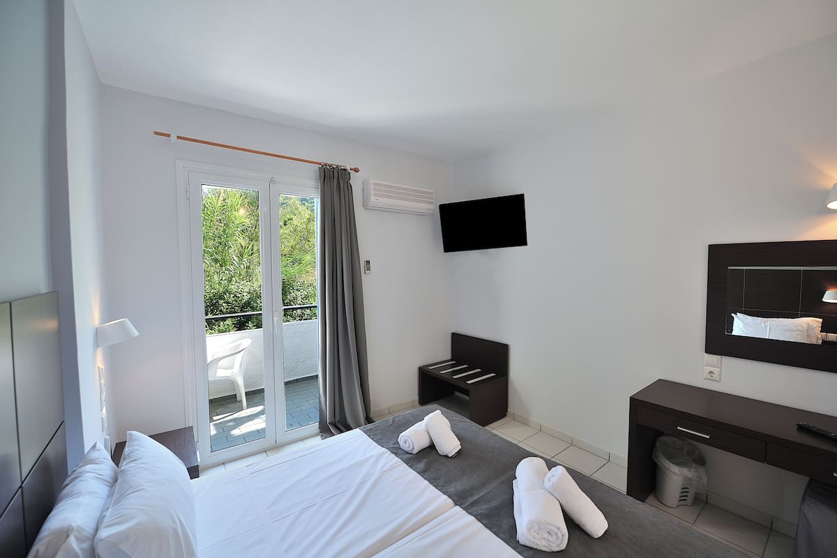 A hotel room with a bed, a desk, a TV, and a balcony with a chair.