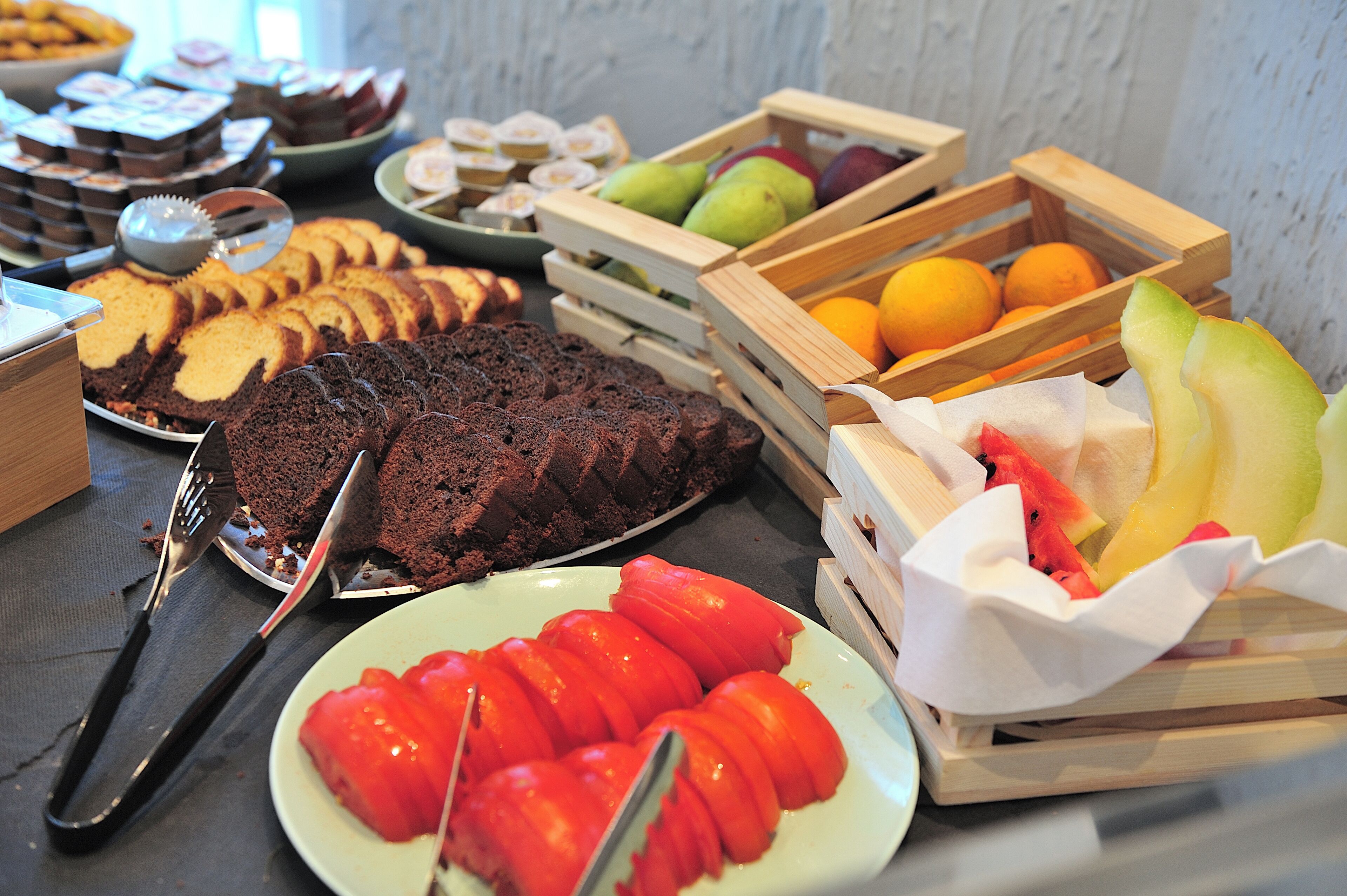 A buffet table with various food items including sliced bread, cakes, fruits, and vegetables.