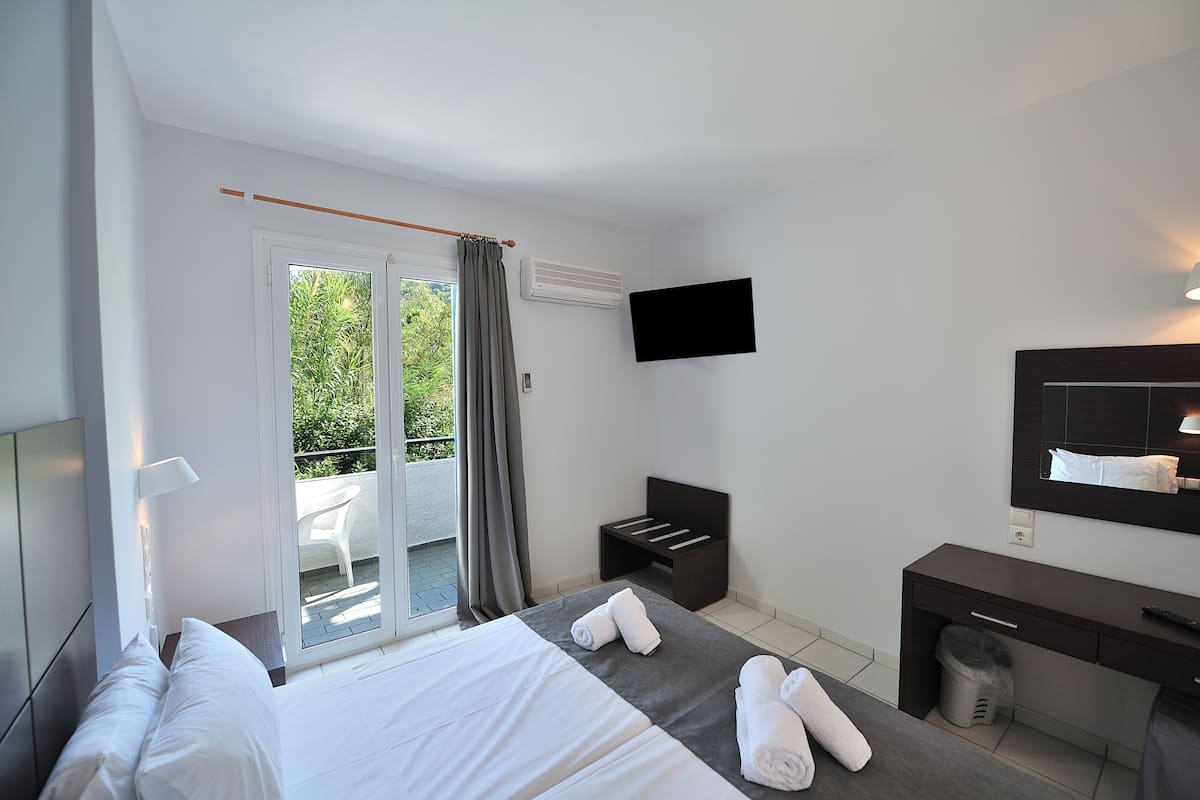 A hotel room with a bed, a desk, a TV, and a balcony with a chair.