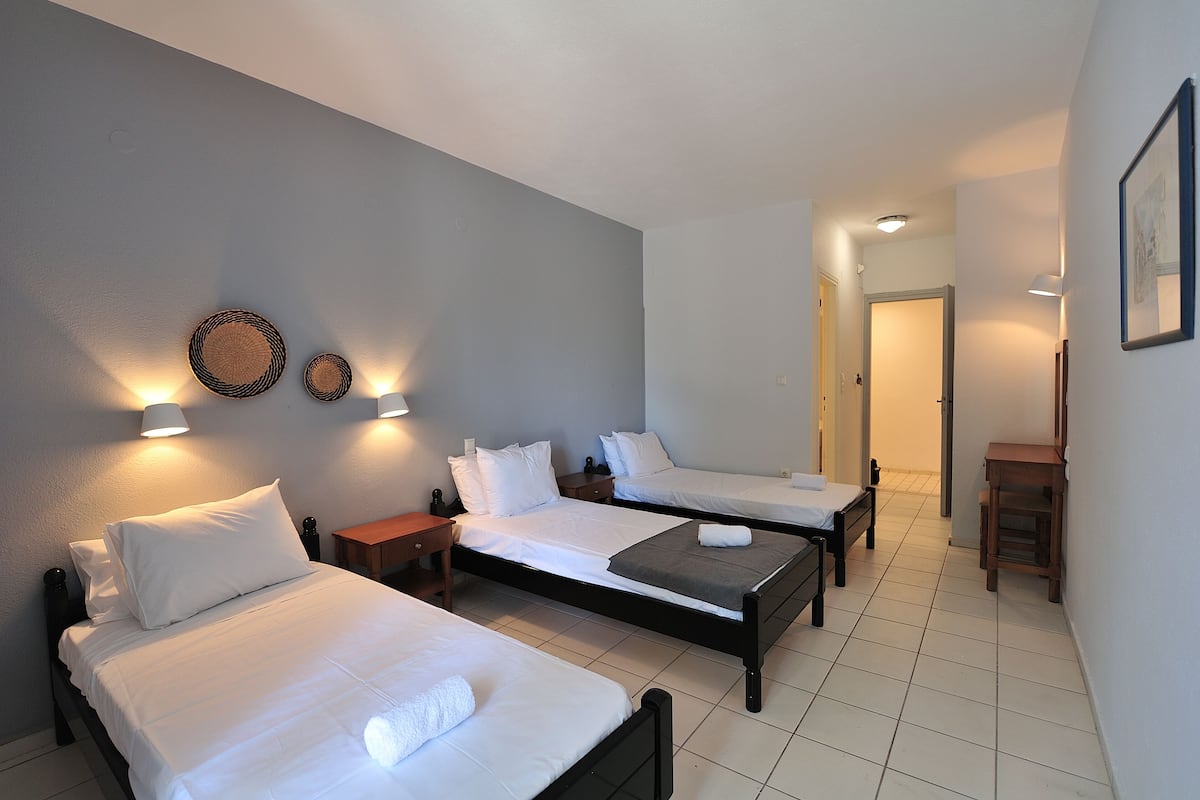 A hotel room with three single beds, a small desk, and a chair.