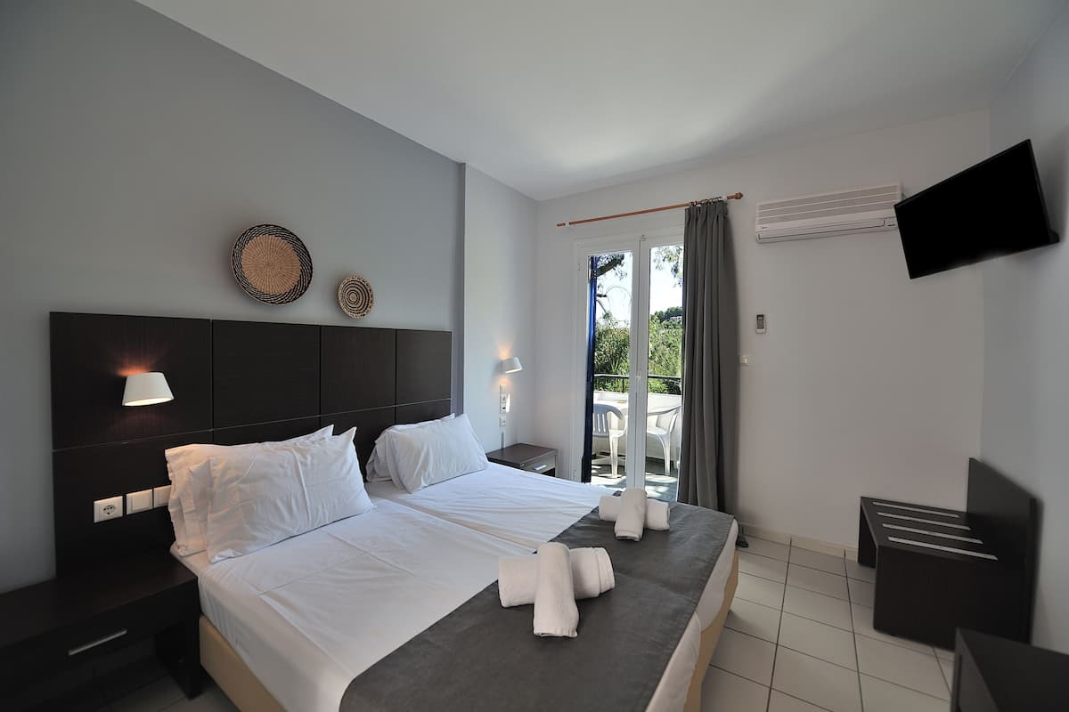A modern hotel room with a large bed, bedside tables, a flat-screen TV, and a balcony with a view.
