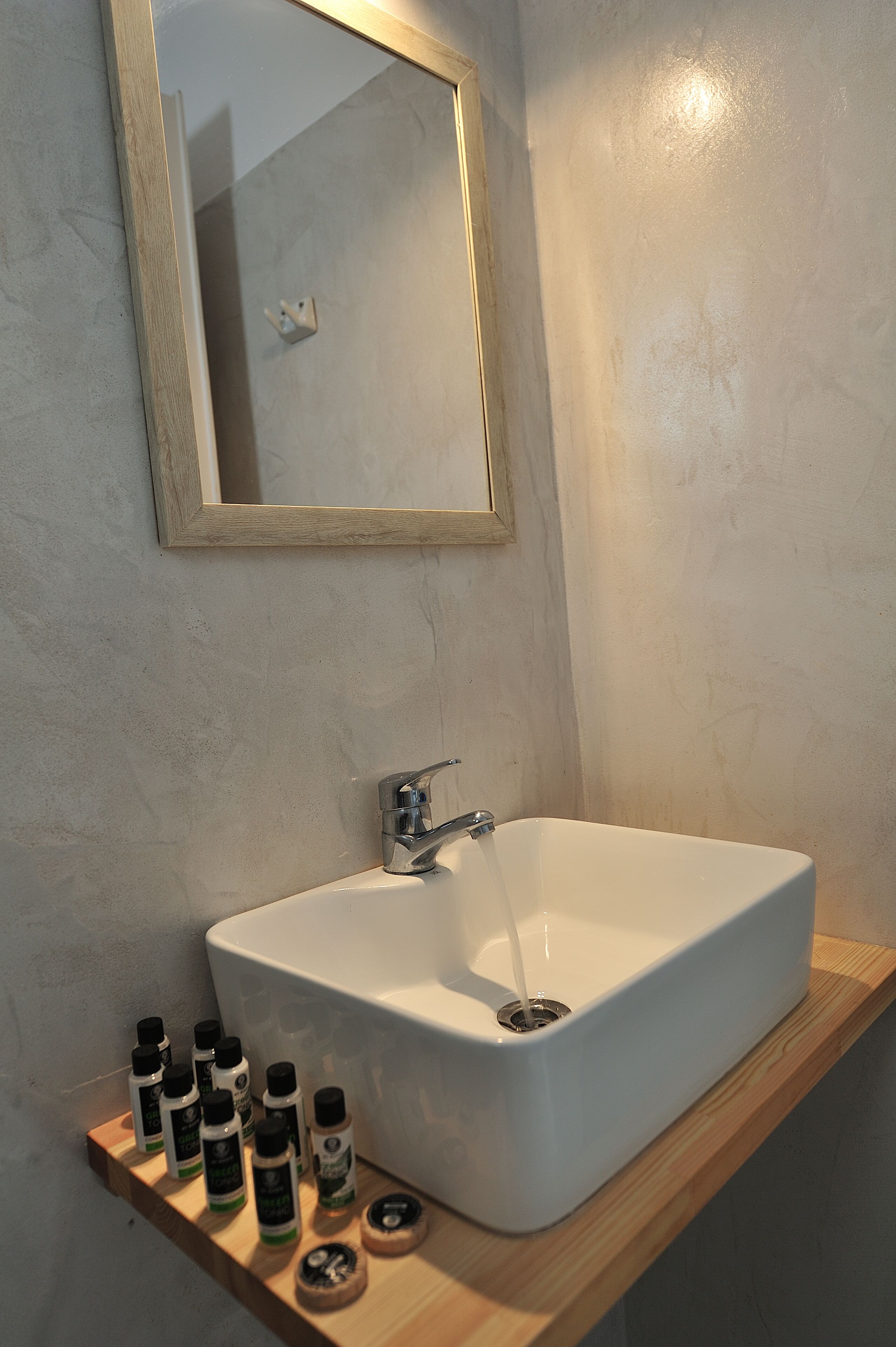 A bathroom with a white sink, a wooden shelf with bottles, and a mirror on the wall.
