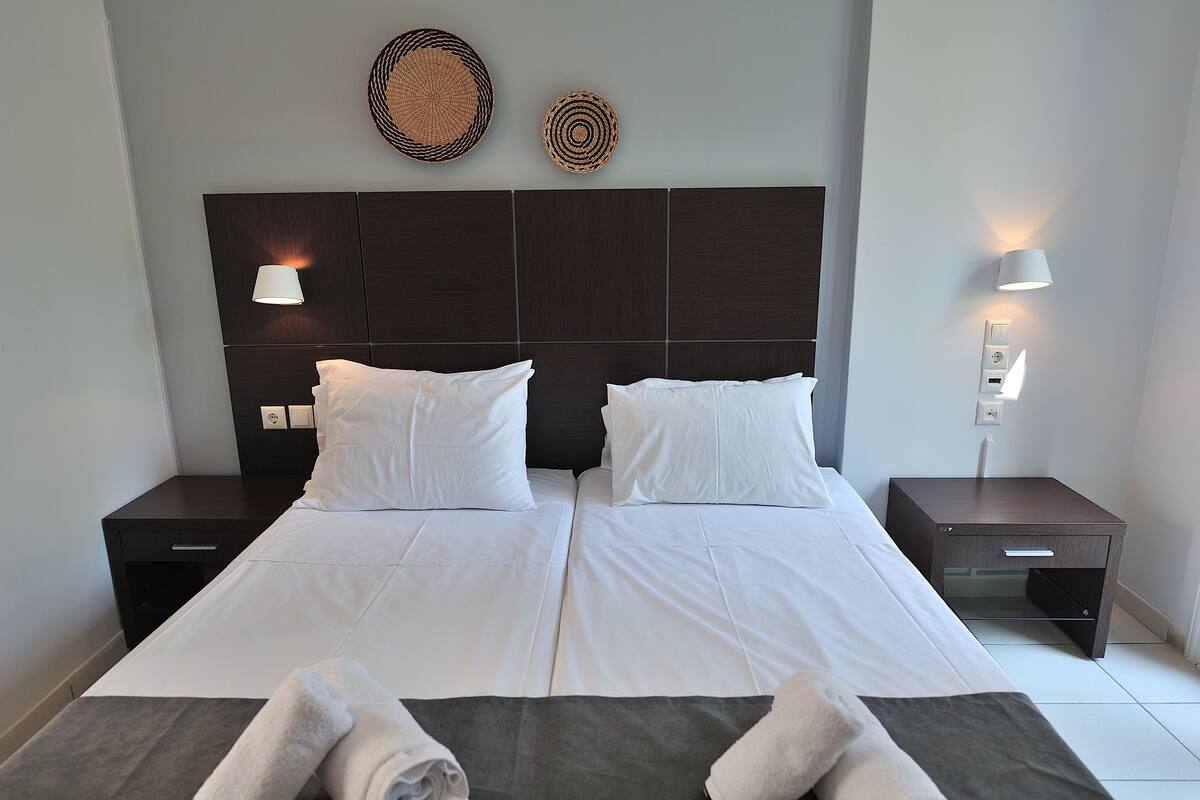 A double bed with white linens, two bedside tables, and wall-mounted lamps.