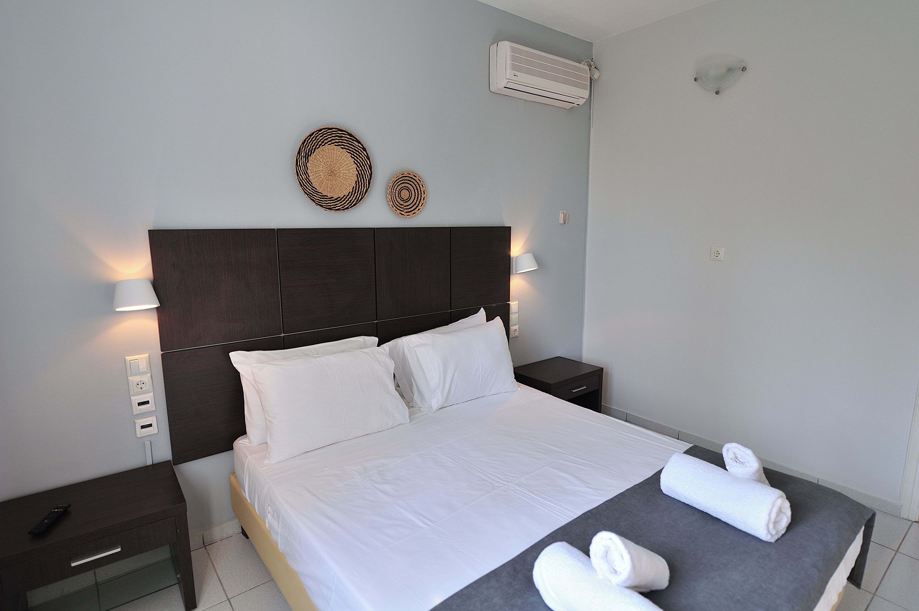 A neatly made bed with white linens, a dark headboard, and two wall-mounted lamps.