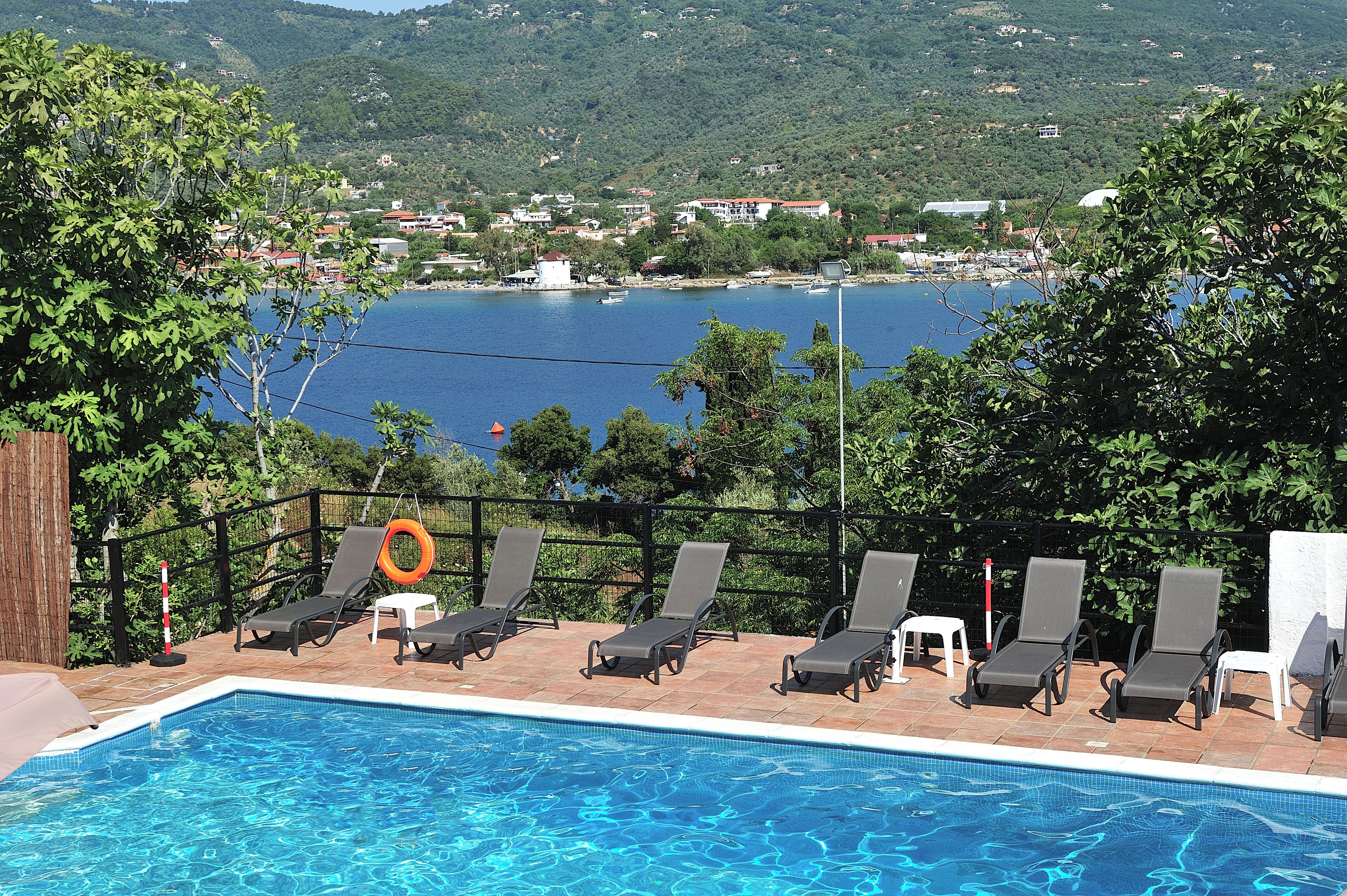 Zona junto a la piscina con sillones de descanso y vista a un lago y un pueblo al fondo.