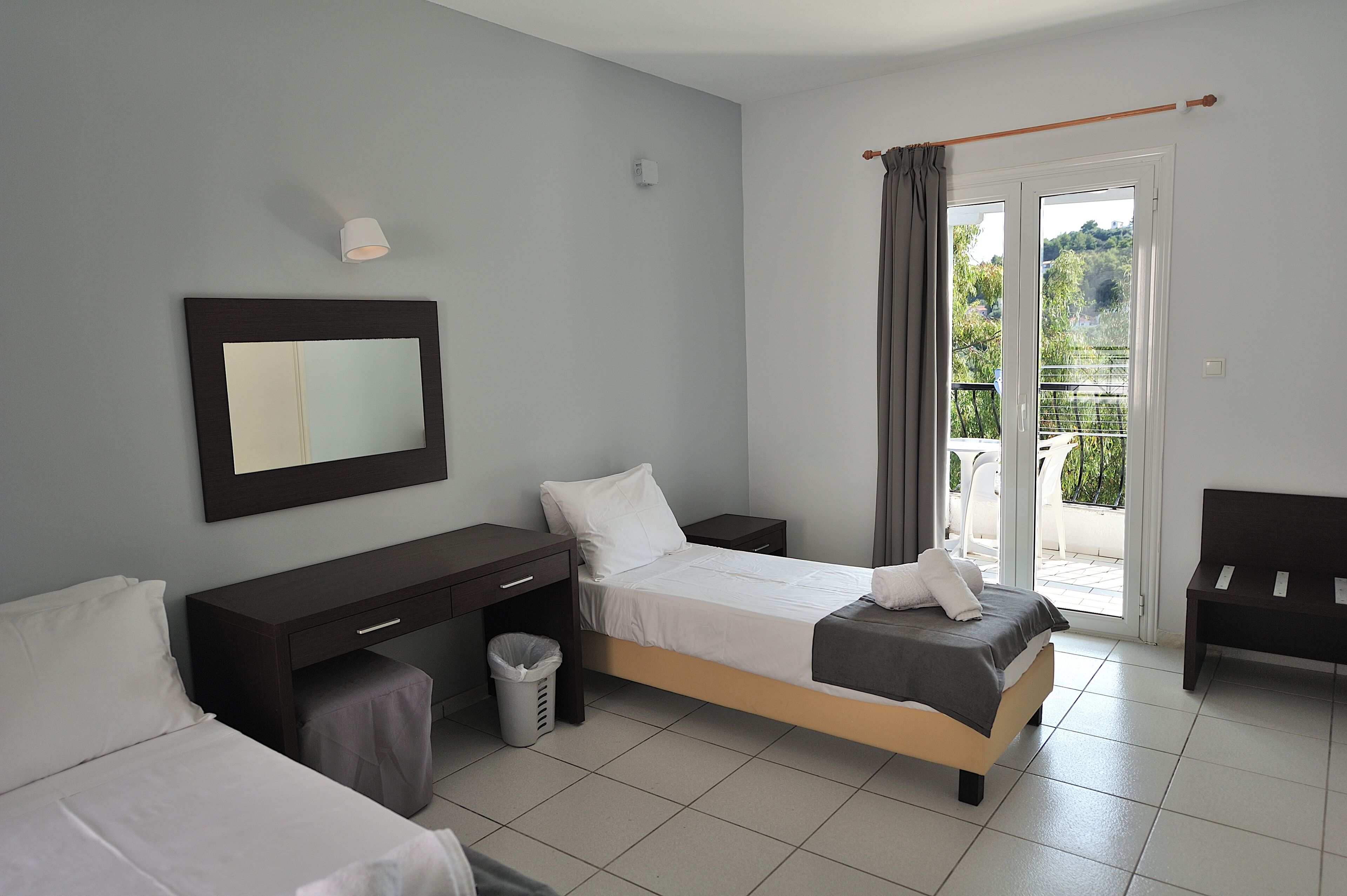 A bedroom with two beds, a desk, a chair, and a balcony with a view.