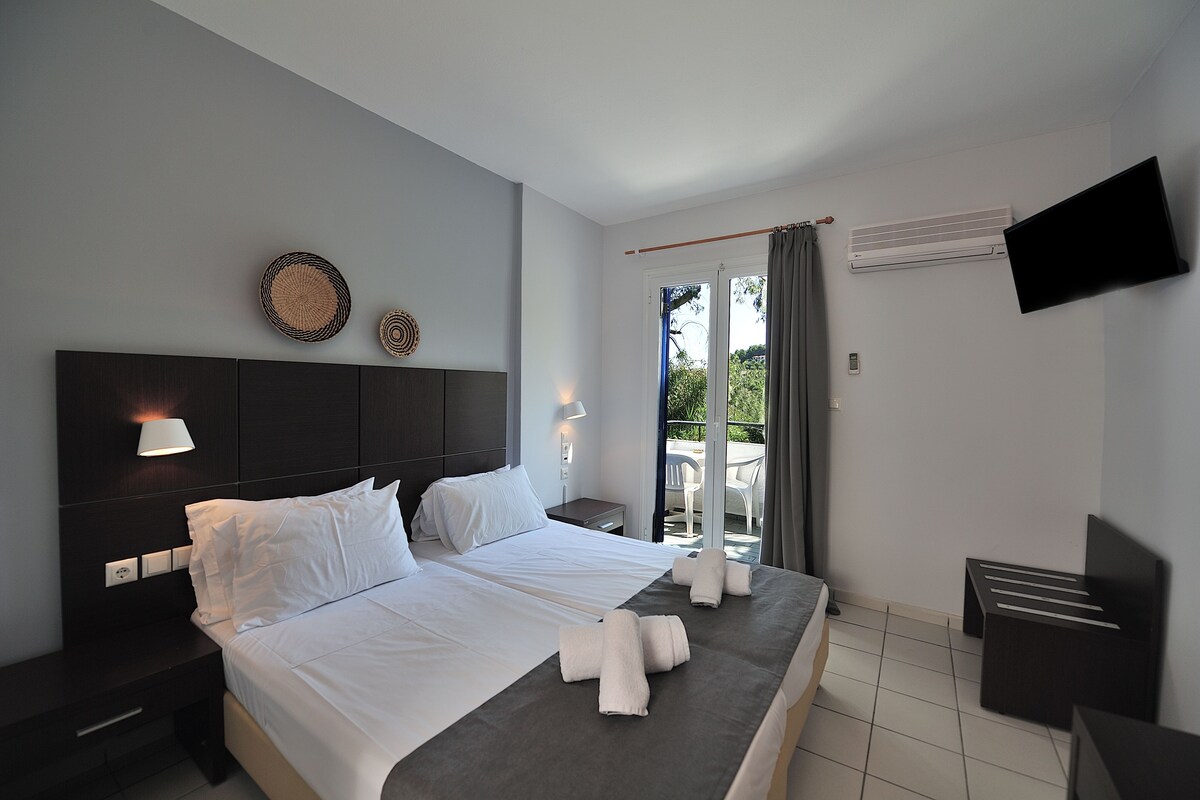 Quarto de hotel moderno com uma cama grande, mesas de cabeceira, televisão de tela plana e varanda com vista.