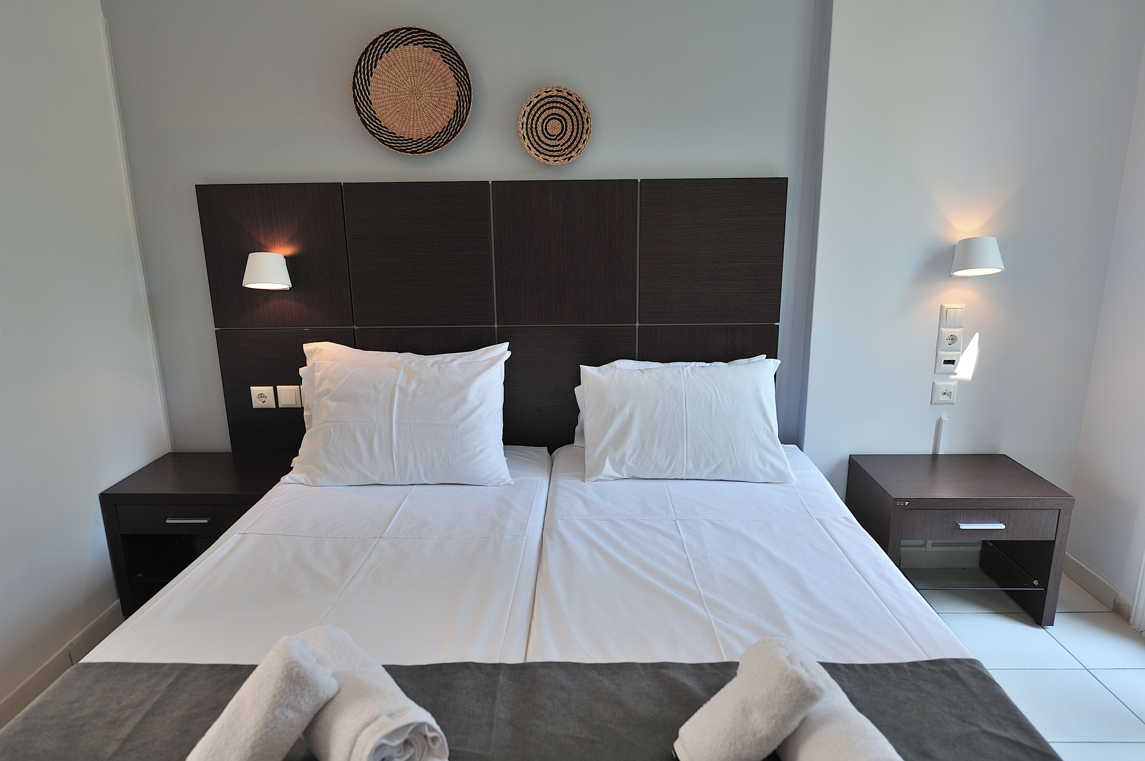 A double bed with white linens, two bedside tables, and wall-mounted lamps.