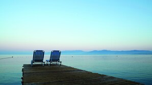 A wooden pier with two striped lounge chairs facing a calm sea and distant mountains. - Aqua Fantasy Aquapark Hotel & Spa - All Inclusive (Selçuk)