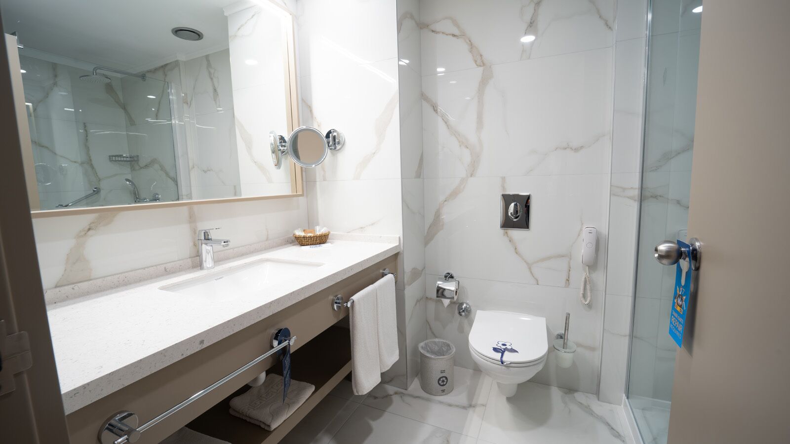 Un baño moderno con tocador de mármol, cabina de ducha de vidrio y un inodoro con un adhesivo floral azul.