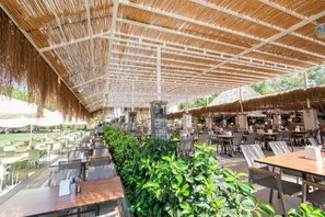 An outdoor dining area with thatched roofs, wooden tables, and chairs. - Aqua Fantasy Aquapark Hotel & Spa - All Inclusive (Selçuk)