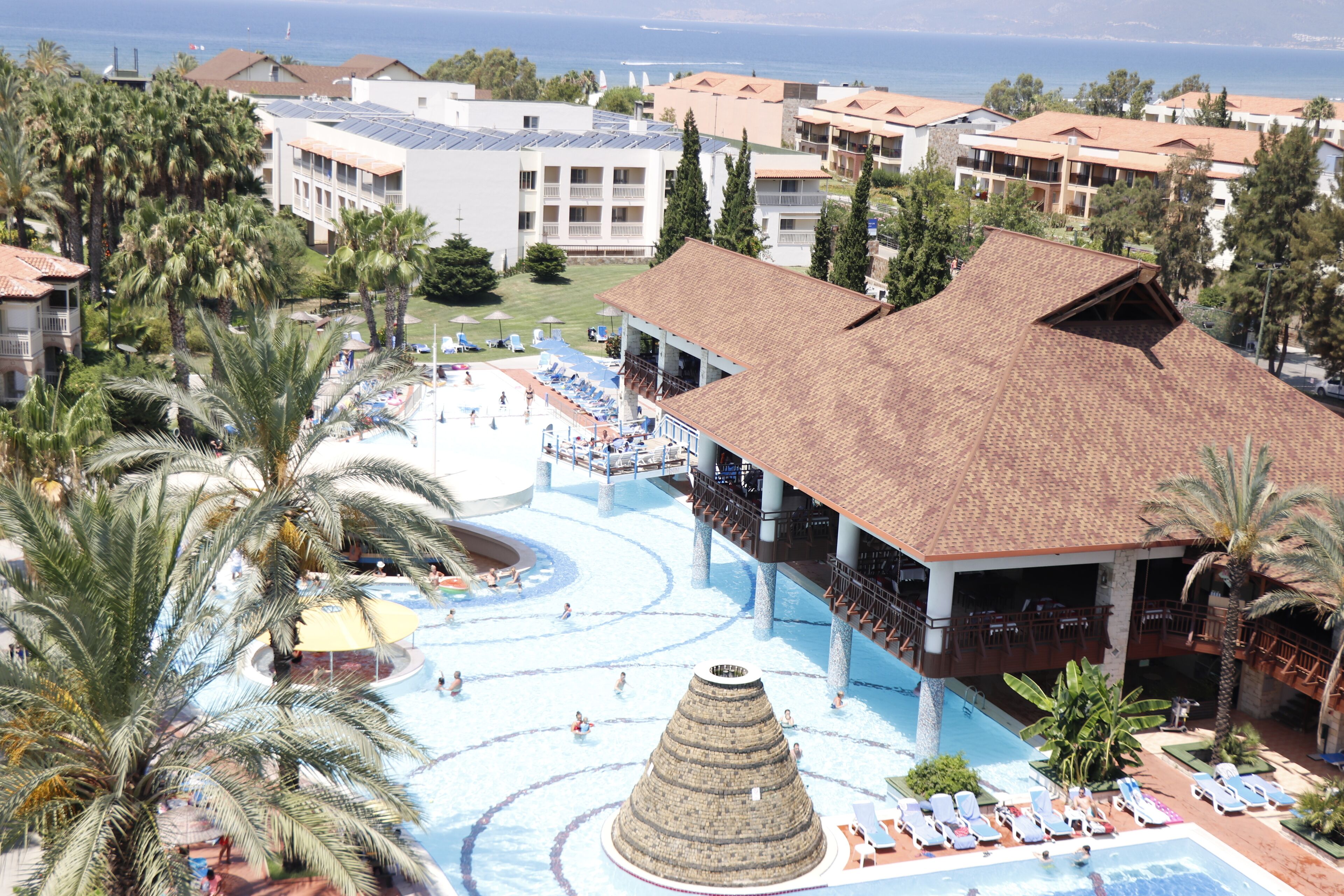A resort with a central pool, multiple lounge areas, and a view of the sea.