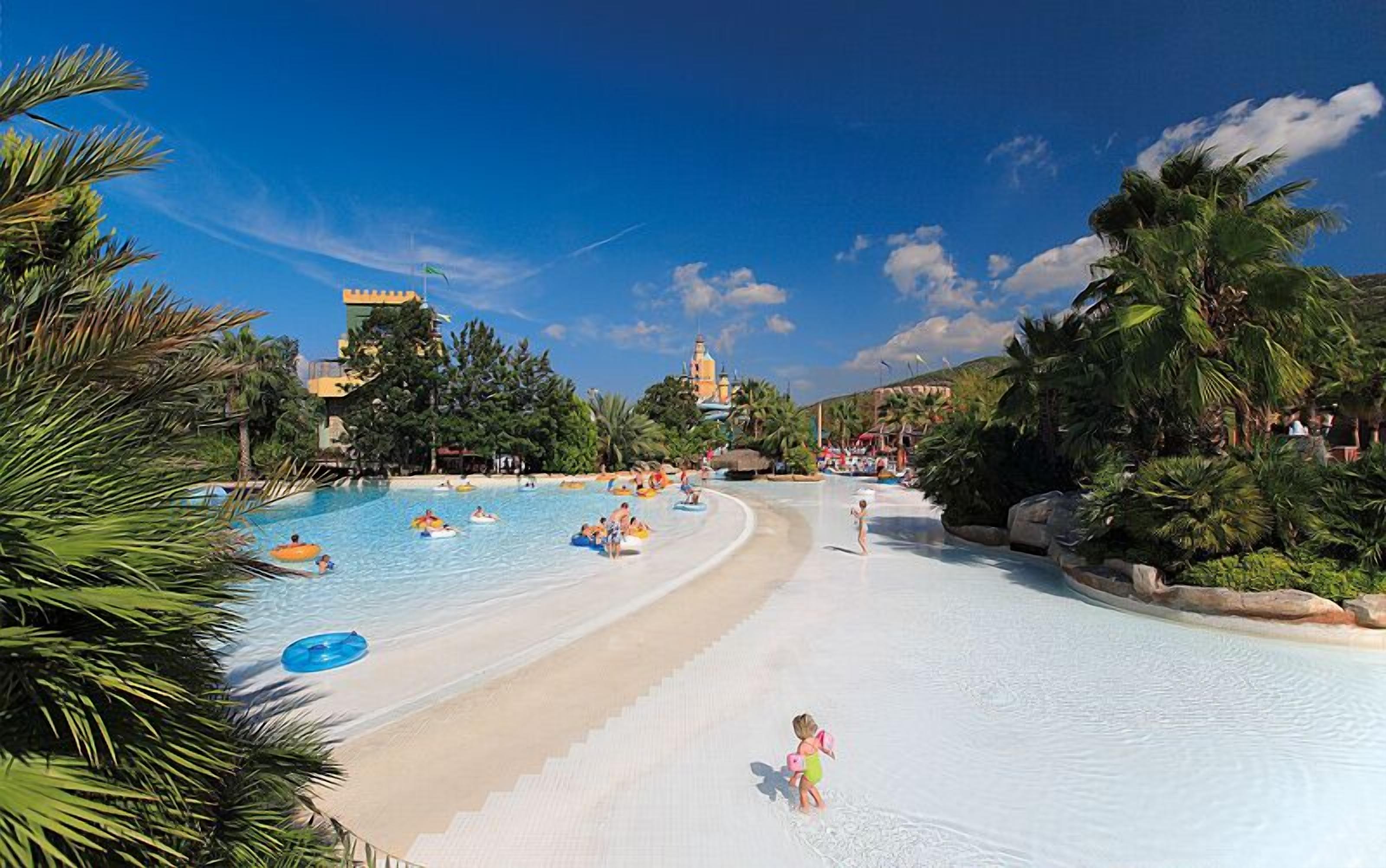 A water park with a sandy beach area, water slides, and palm trees.