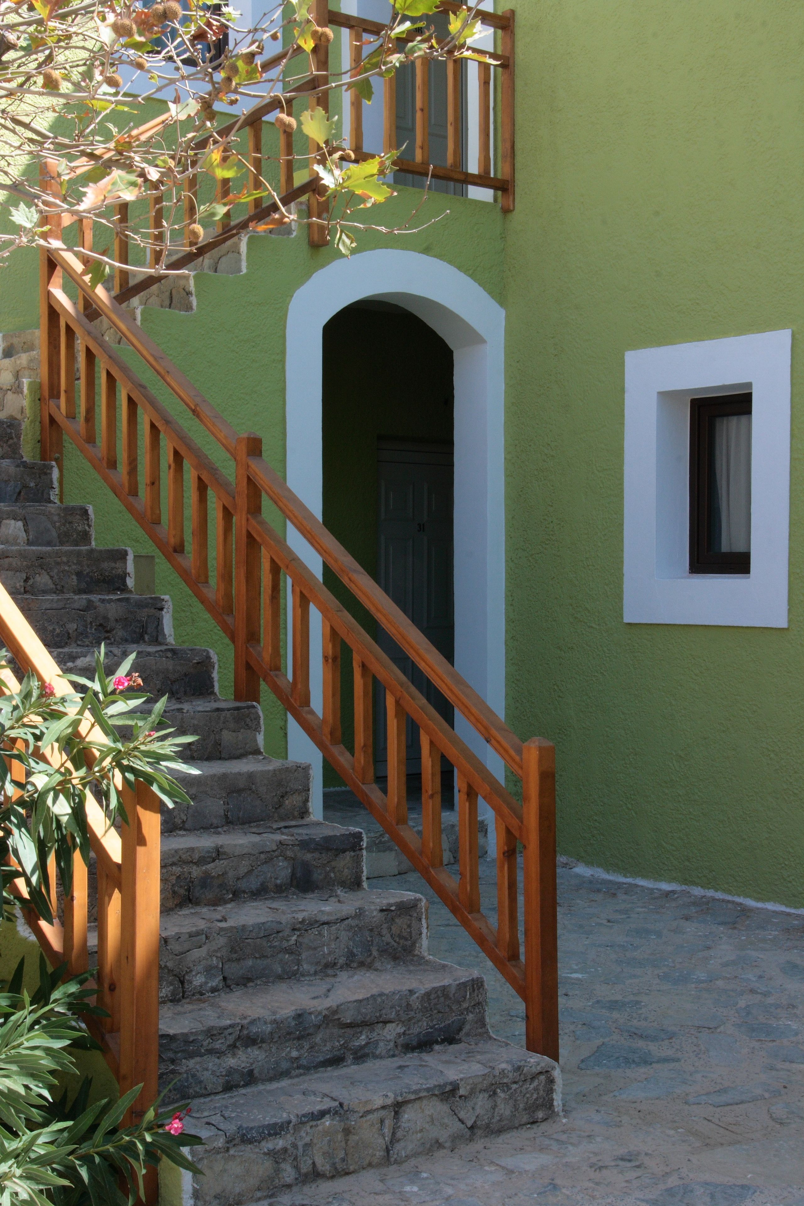 Una escalera con barandillas de madera que lleva a un edificio verde con una puerta de marco blanco y una pequeña ventana.