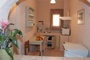 A compact kitchen with a dining table, chairs, a small refrigerator, and a sink. - Perla Apartments (Malevizi)