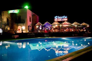 A poolside view of a hotel with a neon sign, a restaurant bar, and a pool reflecting the surroundings. - Aparthotel Siesta Beach Bodrum (Bodrum)
