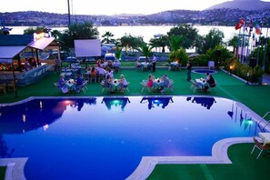An outdoor pool area with tables and chairs, surrounded by greenery and flags. - Aparthotel Siesta Beach Bodrum (Bodrum)