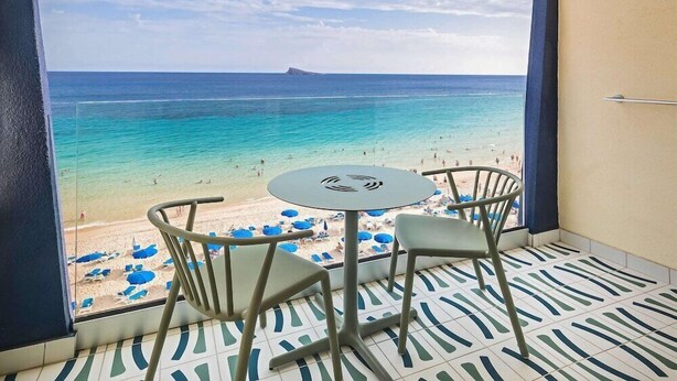 A balcony with a view of a beach and ocean, featuring a table and chairs. - Selomar (Benidorm)