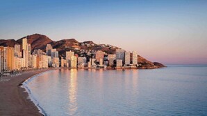 A coastal cityscape with high-rise buildings, a beach, and a mountain backdrop. - Selomar (Benidorm)