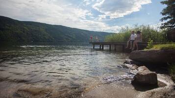 A lake with a wooden dock extending into the water, surrounded by greenery and hills.