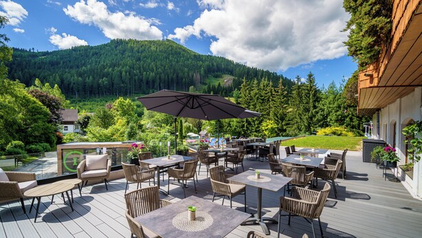 Une terrasse extérieure avec des tables et des chaises, entourée de verdure et de montagnes.